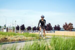 A cyclist in a black outfit rides through a green park on a sunny day, surrounded by nature and city
